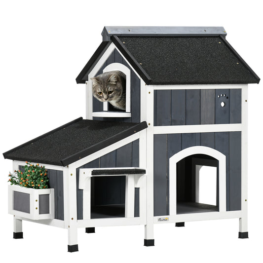 grey tabby cat in a two-story wooden cat house with black shingle roof, white trim, and planter box